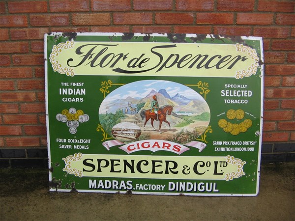 A green enamel advertising sign for Flor de Spencer cigars, showing a mounted rider in a mountain landscape and medals from international exhibitions